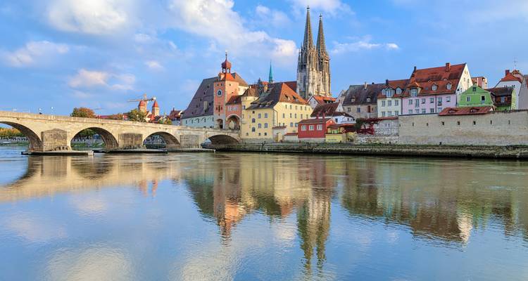 Puente de Piedra y el colorido horizonte medieval de Regensburg reflejado en las tranquilas aguas del río Danubio.