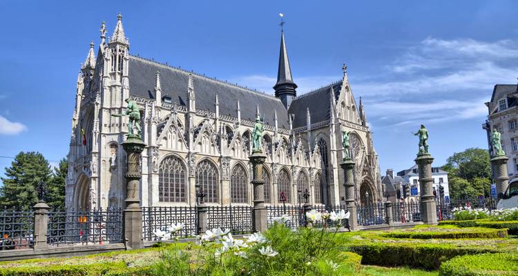 Iglesia gótica Notre-Dame du Sablon en Bruselas con jardín florecido en primer plano bajo cielo azul.