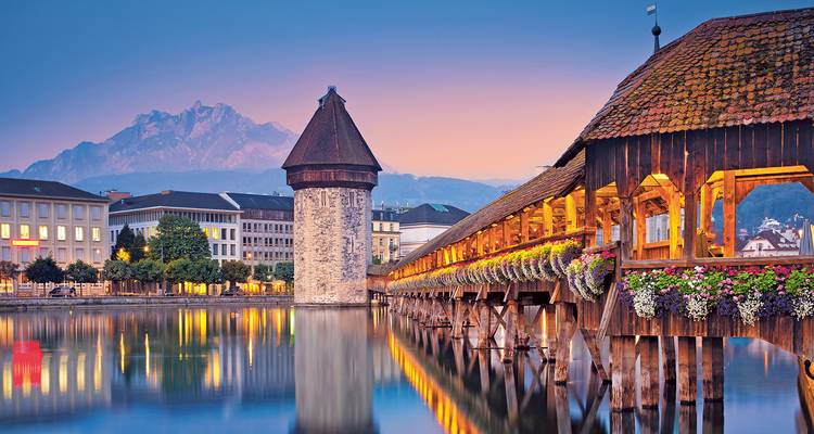 Lueur du soir sur le pont de la Chapelle en bois de Lucerne avec silhouette de montagne et reflets du lac.