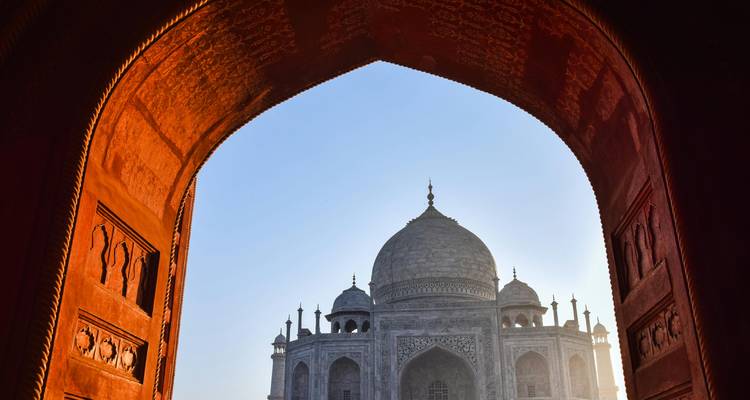El Taj Mahal resplandece a través de un arco de arenisca roja al amanecer.