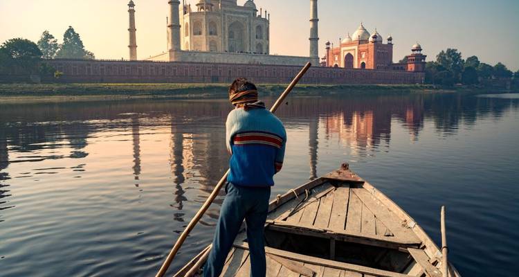 Un barquero rema en el río Yamuna con el resplandor del amanecer sobre el Taj Mahal al fondo.