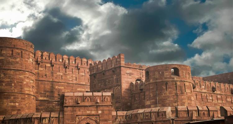 Enormes murallas y bastiones de arenisca roja del Fuerte de Agra bajo un cielo dramático nublado.