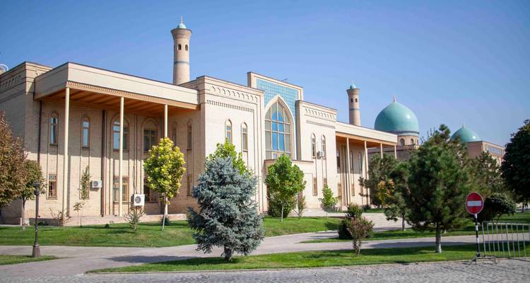 Complexe islamique moderne en brique avec dômes turquoise et minaret élancé le long d'une rue paysagée