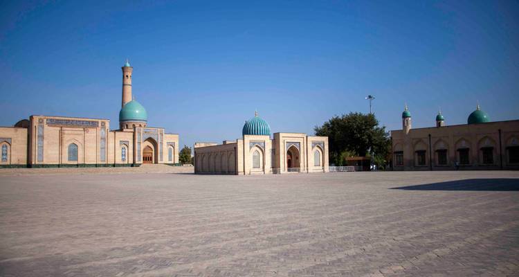 Large place vide avec des bâtiments de médersa et des dômes turquoise sous un ciel bleu clair