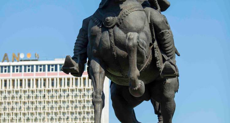 Statue équestre en bronze d'Amir Timur dressée contre la façade d'un hôtel moderniste sous un ciel bleu dégagé.