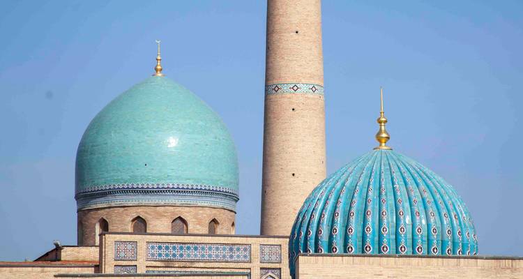 Deux dômes turquoise jumeaux et un minaret de brique élancé du complexe Hazrati Imam s'élevant dans un ciel sans nuages.