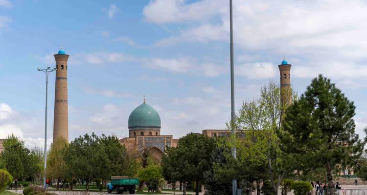 Cadre de parc avec arbres et lampadaires encadrant les dômes et minarets de Hazrati Imam sous des nuages mitigés.