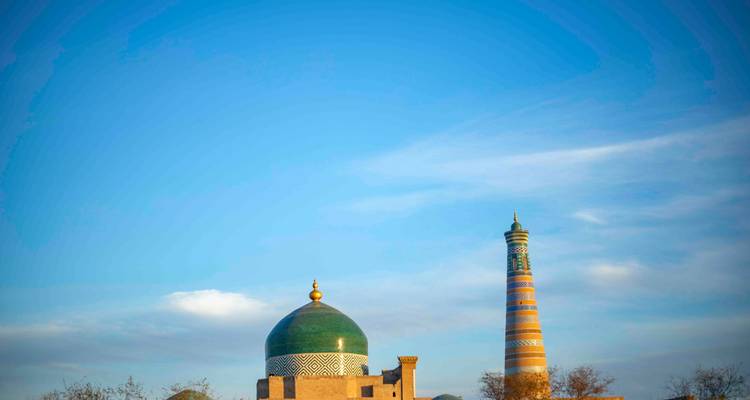 Dôme isolé aux tuiles vertes et minaret aux rayures colorées de Khiva s'élevant dans un vaste ciel bleu.