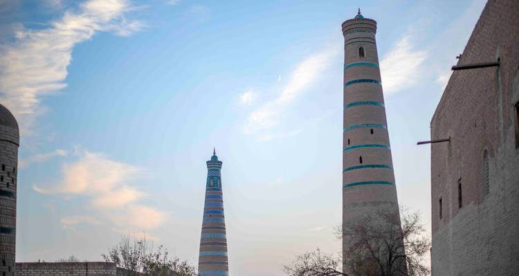Minarets jumeaux de Khiva se profilant contre un ciel de soirée pastel avec un faible croissant de lune.