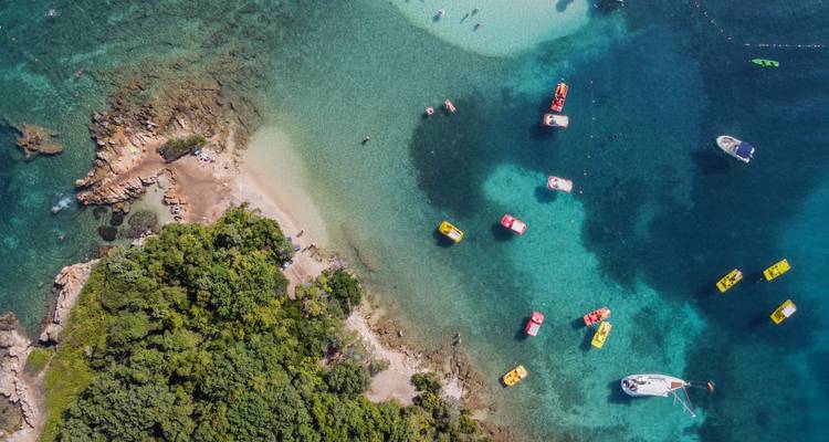 Luchtfoto van turquoise baaien met boten, kajaks en een weelderig groen schiereiland