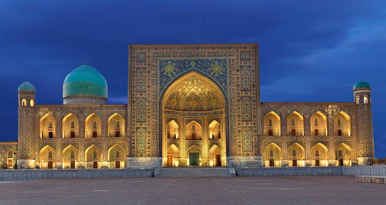 Iluminación nocturna de las ornamentadas madrasas de la Plaza Registán resplandeciendo contra un cielo azul profundo en Samarcanda