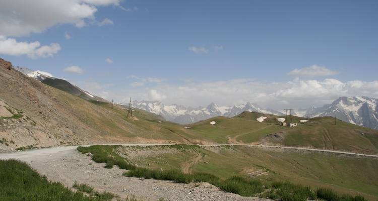 Carretera de tierra a gran altitud serpenteando a través de montañas escarpadas con cimas nevadas y laderas cubiertas de hierba