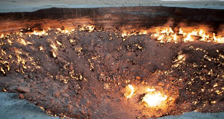 Cráter de gas ardiente de Darvaza con llamas resplandecientes dentro de un vasto foso desértico al anochecer