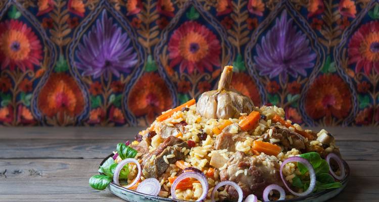 Plato tradicional de plov de Asia Central con arroz, cordero y verduras apilados en un plato ornamentado