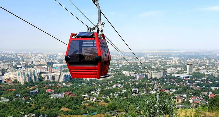 Rote Seilbahn steigt über Almaty auf mit Stadtsilhouette und entfernten Ebenen darunter