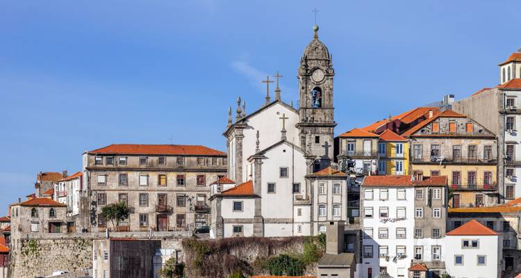 Nahaufnahme eines barocken Kirchturms und umliegender Häuser mit Ziegeldächern unter klarem Himmel in Porto.