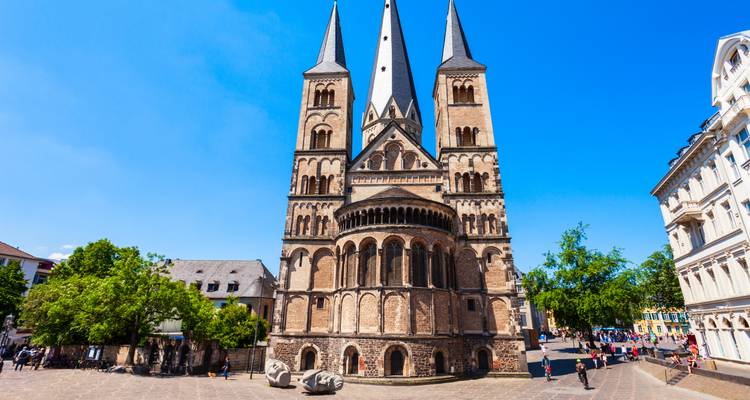 Frontansicht der romanischen Bonner Münsterkirche mit klarem blauen Himmel und Fußgängern auf dem Platz.
