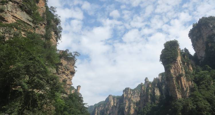Acantilados escarpados de arenisca y árboles verdes bajo un cielo azul con nubes en Zhangjiajie.