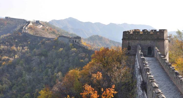 Torre de vigilancia de piedra y murallas de la Gran Muralla serpenteando sobre colinas de colores otoñales.