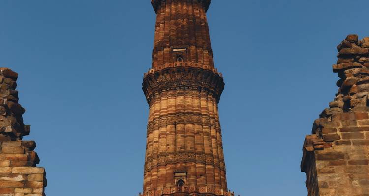 Toma en contrapicado del alto minarete Qutub Minar de arenisca roja enmarcado por arcos en ruinas