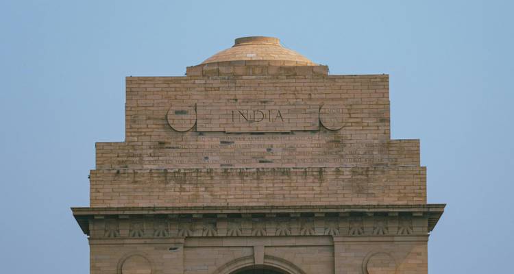 Vista cercana de la sección superior de India Gate con la palabra grabada 'INDIA' bajo un cielo despejado