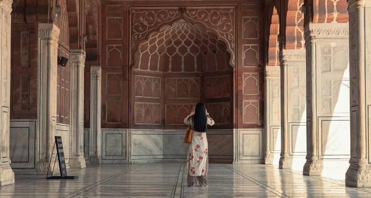 Mujer en vestido floral fotografiando dentro de un gran salón de mármol y arenisca roja de estilo mogol