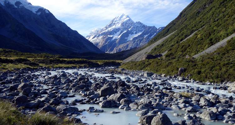Sneeuwbedekte Mount Cook die oprijst achter een rotsachtige alpiene riviervallei