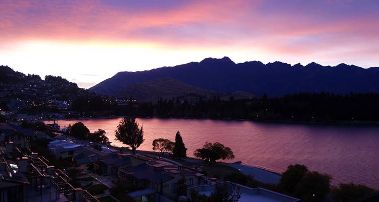 Paarse en oranje dageraadlucht boven een kalm meer en bergsilhouet bij Queenstown