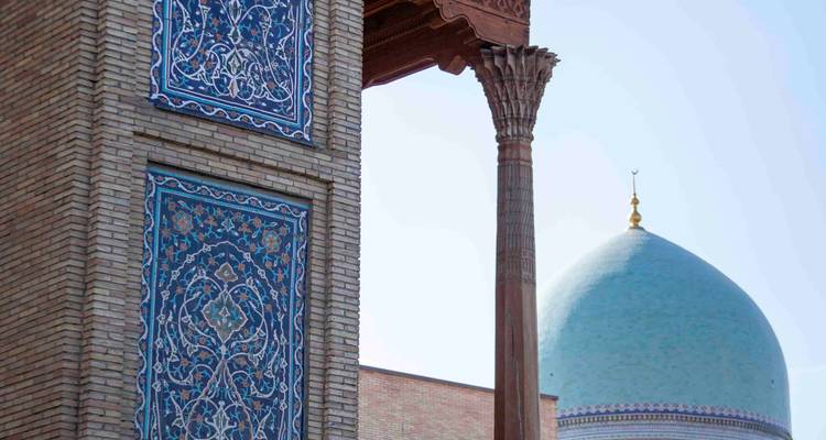 Colonne de brique ornée de carrelage bleu à côté d'un dôme turquoise lointain sous un ciel dégagé.