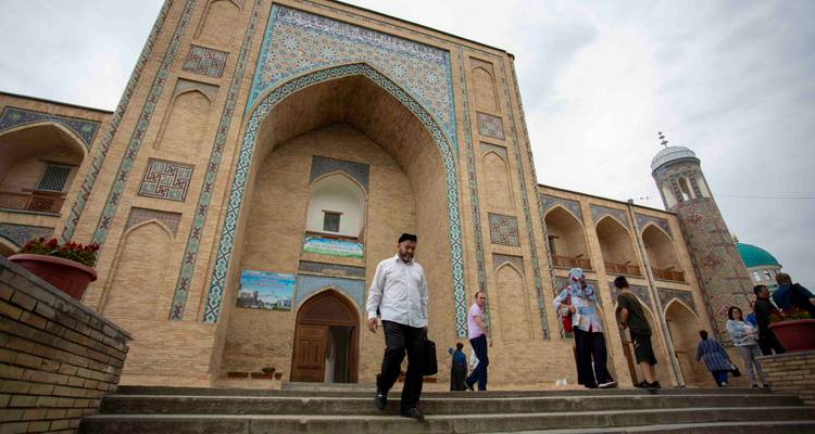 Des visiteurs descendant les marches d'une entrée de médersa carrelée par une journée nuageuse.