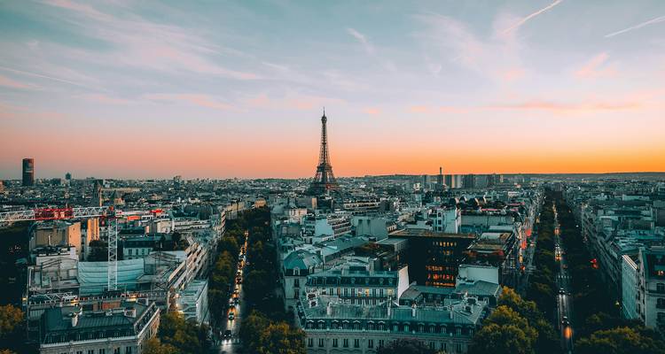 Panoramic view of Paris at dusk with the Eiffel Tower silhouetted against a colorful sky.