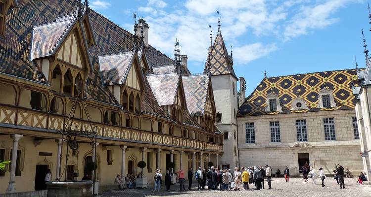Visitors gather in the courtyard of the medieval Hospices de Beaune with its colorful tiled roofs.