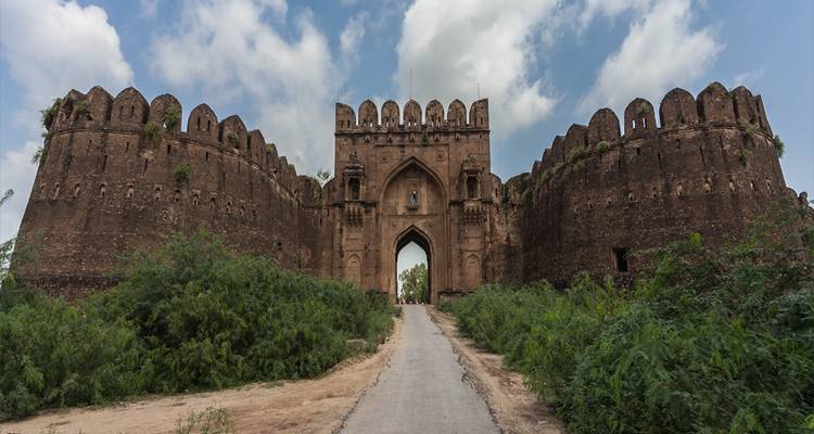 Massives steinernes Festungstor mit flankierenden runden Bastionen, das eine schmale Zufahrtsstraße bewacht.