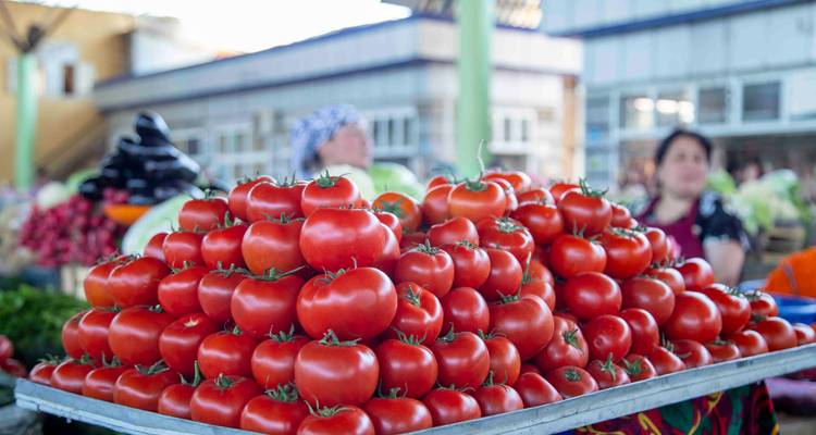 Tas de tomates rouges mûres sur un marché en plein air avec des vendeurs flous en arrière-plan.