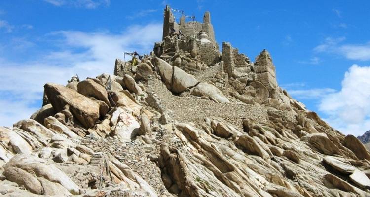 Verfallene Steinfestung thront auf zerklüfteter Felsklippe unter strahlend blauem Himmel.