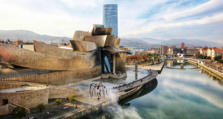 Musée Guggenheim Bilbao futuriste au bord de la rivière Nervión avec paysage urbain et collines lointaines.