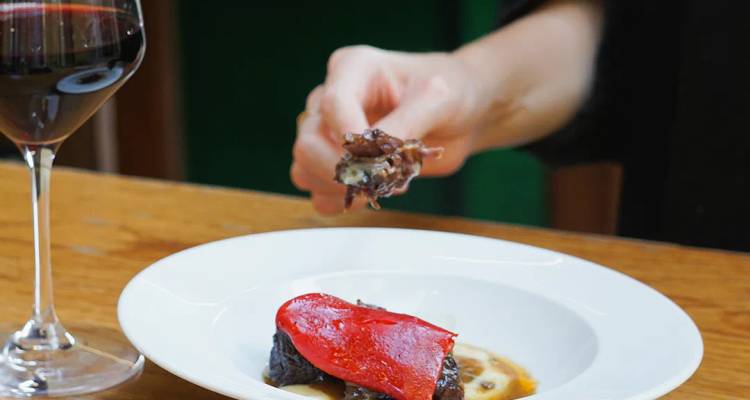 Un delicioso pintxo gourmet siendo comido con una copa de vino tinto a su lado.