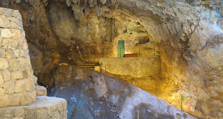 Interior iluminado de una cueva de piedra caliza con pasarelas y formaciones rocosas.