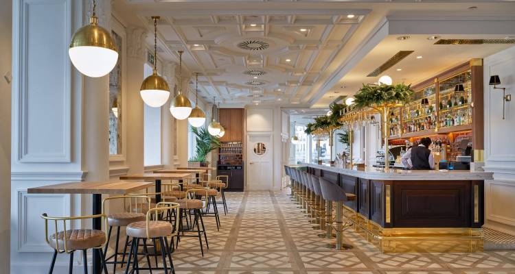 Café-bar moderno y luminoso con piso con diseño, accesorios de latón y un barman trabajando.
