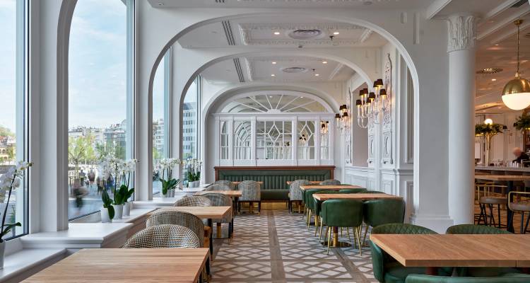 Restaurante luminoso con grandes ventanas arqueadas, sillas verdes y piso de azulejos con diseño.