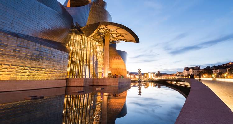 Vista nocturna del Museo Guggenheim Bilbao con sus curvas de titanio reflectante espejadas en el agua.