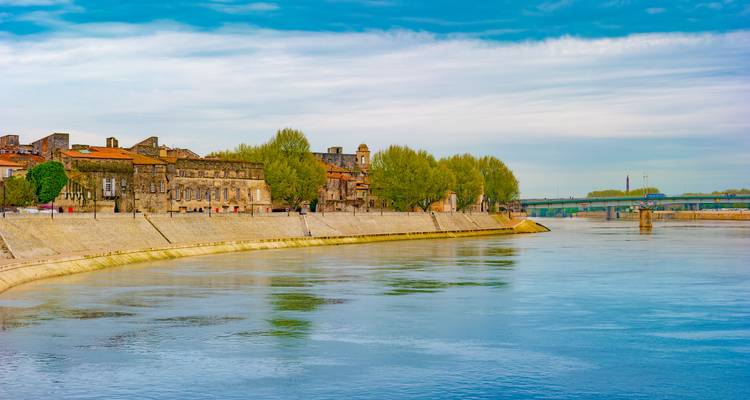 Rustige rivierscène aan de Rhône nabij Avignon met historische stenen gebouwen en lommerrijke bomen weerspiegeld in het kalme water.