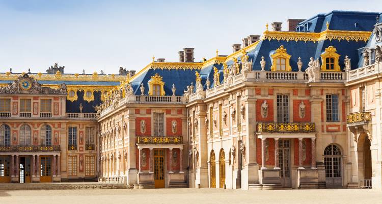 Prunkvolle Außenansicht des Schlosses Versailles mit goldverzierten blauen Dächern unter klarem Himmel.