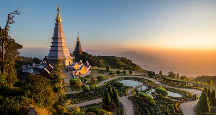 Zwillingsstupas des Doi Inthanon Nationalparks überblicken gepflegte Gärten bei Sonnenaufgang mit nebligen Bergen in der Ferne.