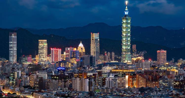 Nachtbeeld van de verlichte skyline van Taipei gedomineerd door Taipei 101 tegen donkere heuvels.