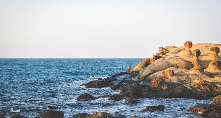 Rotsachtige kustlijn en diepblauwe oceaan onder bleek avondlicht.
