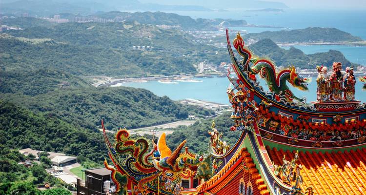 Levendig met draken versierd tempeldak met uitzicht op weelderige bergen en blauwe baai.