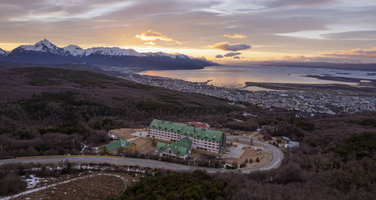 Luchtfoto bij zonsondergang over Ushuaia, besneeuwde toppen en het Beaglekanaal met warm licht.