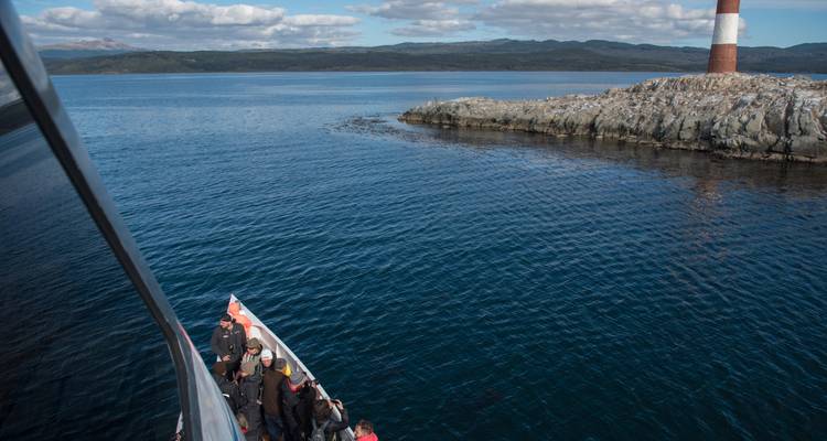 Rondvaartboot met passagiers nadert een kleine vuurtoren op rotsachtig eiland in het Beaglekanaal.