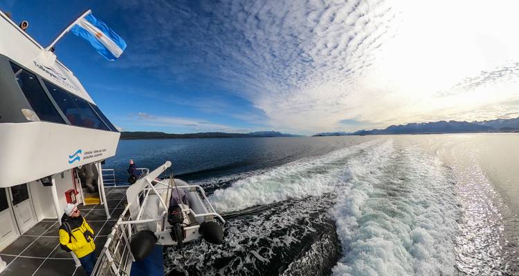 Hogesnelheids catamaran laat schuimend kielzog achter onder dramatische wolkenpatronen met Argentijnse vlag wapperend.